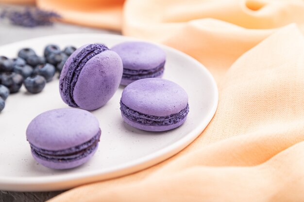 Lila Makronen oder Makronenkuchen mit Blaubeeren auf weißer Keramikplatte auf grauem Betonhintergrund.