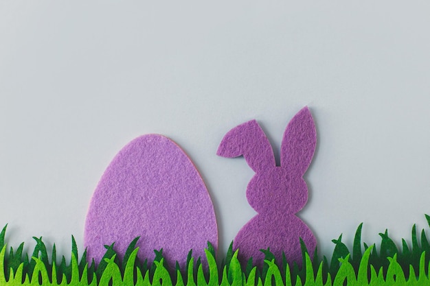 Lila Osterei und Hase im Gras auf grauem Hintergrund flach lag Platz für Text Frohe Ostern