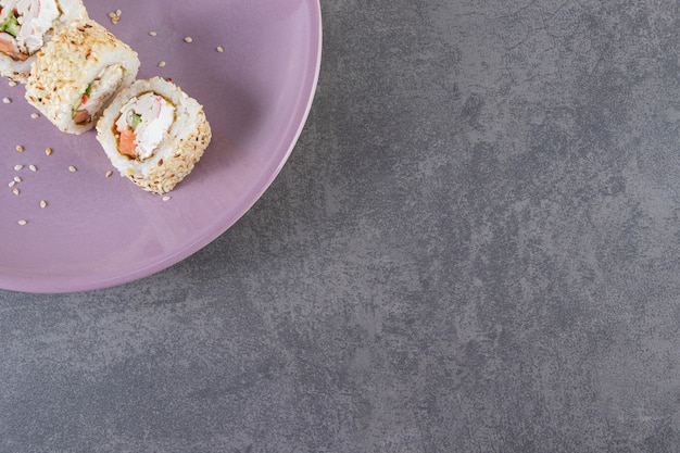 Lila platte von sushi-rollen mit sesam auf steinhintergrund.