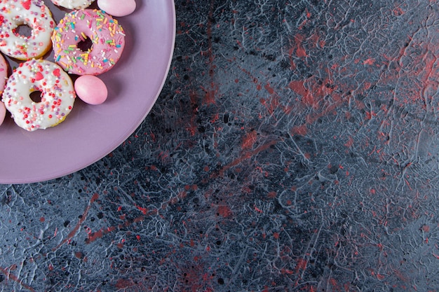 Lila Teller mit bunten köstlichen Donuts auf dunkler Oberfläche.