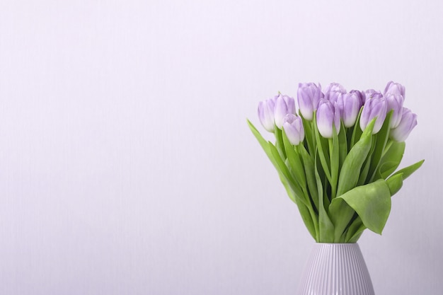 Lila Tulpenblumenstrauß in der Vase auf grauem Hintergrund.