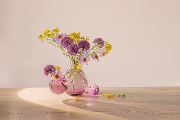lila und gelbe Blumen in Glas moderne Vase auf einem Holztisch im Sonnenlicht