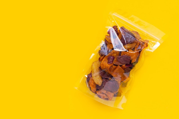 Lila und gelbe Süßkartoffelchips in Plastiktüte auf gelbem Hintergrund.