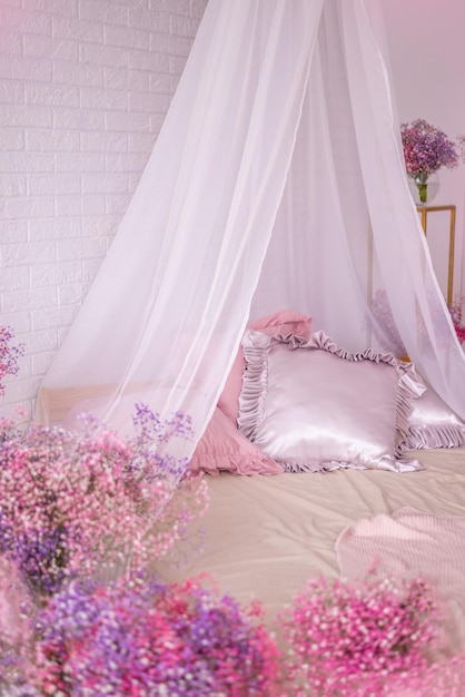 Lilac de cetim e travesseiros cor-de-rosa com flocos em uma cama com um dossel branco flores de gipsófila rosa decoram o quarto.