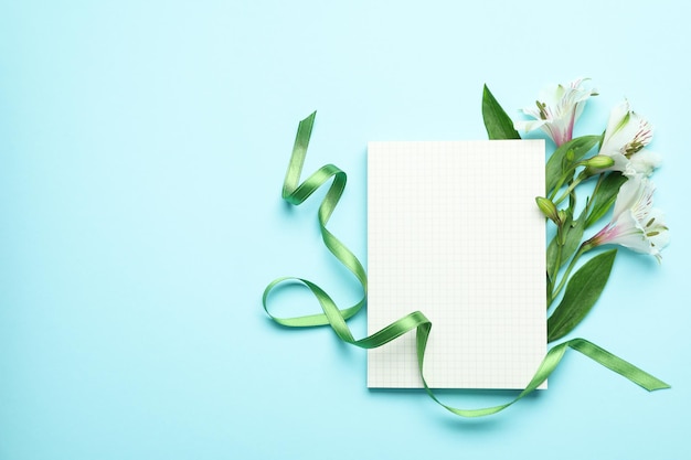 Lilien, grünes Band und leeres Blatt auf blauem Hintergrund