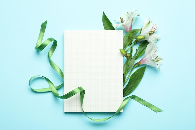 Lilien, grünes Band und leeres Notizbuch auf blauem Hintergrund