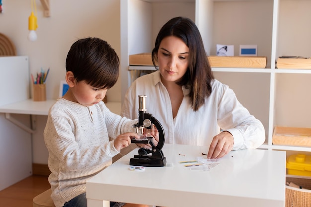 Lillte Kid explorando la ciencia con un microscopio y la ayuda de una madre o un maestro. Educación en el hogar. Comunidad de aprendizaje. Escuela Montessori