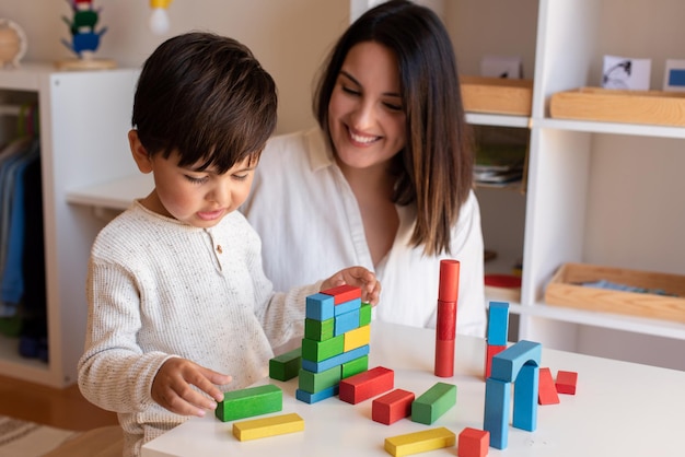 Liltle Preschooler Kid brincando com blocos de madeira e professor educador ajuda. Homeschooling. Comunidade de Aprendizagem. Escola Montessori