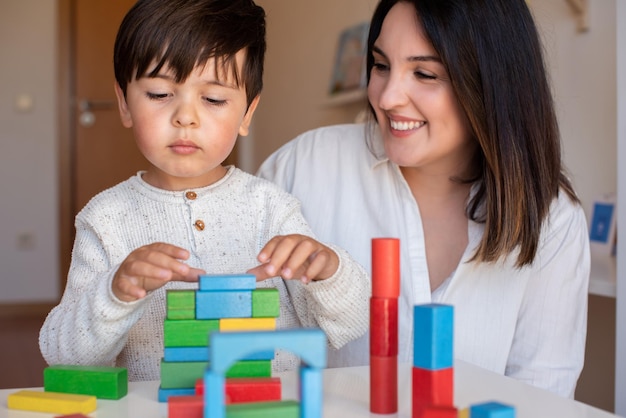 Liltle Preschooler Kid spielt mit Holzklötzen und Lehrer-Educador-Hilfe. Homeschooling. Lerngemeinschaft. Montessori-Schule