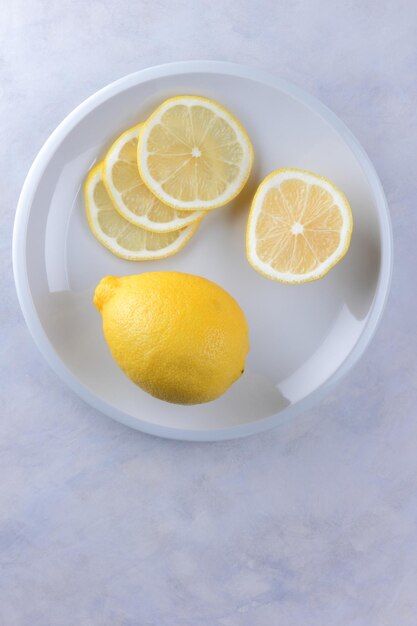 Limão inteiro e fatias de limão em um prato branco Composição de frutas cítricas em fundo cinza claro Frutas tropicais orgânicas frutas cítricas vitamina C Closeup