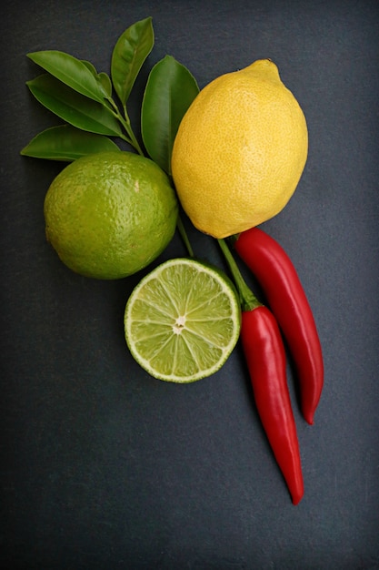 Foto limão, limão e pimenta vermelha em uma superfície preta