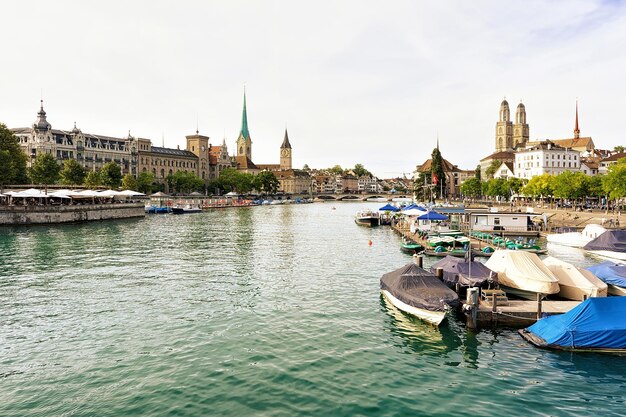 Limmat River Quay com barcos e três igrejas principais de Zurique - Grossmunster, Fraumunster e St Peter Church. Suíça