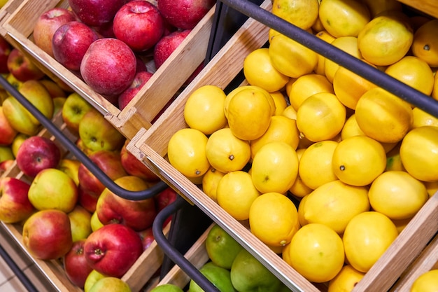 Limões, maçãs vermelhas e verdes em caixas de madeira nas prateleiras das lojas