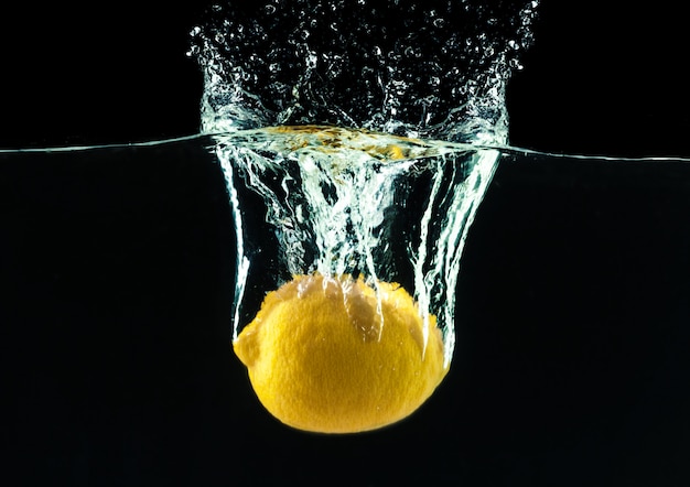 Limón amarillo fresco en salpicaduras de agua sobre fondo negro