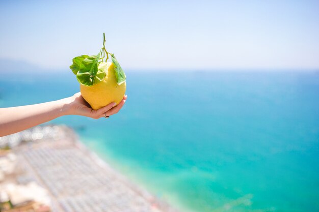 Limón amarillo grande en la mano en el fondo del mar Mediterráneo y el cielo.