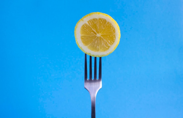 Limón apuñalado en un tenedor de plata en el espacio de copia de primer plano de fondo azul