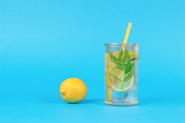 Limón fresco y un vaso de agua con menta y limón sobre un fondo azul.