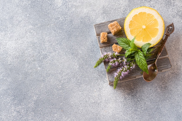 Limón y hojas de menta fresca con flores, el azúcar moreno sobre un gris