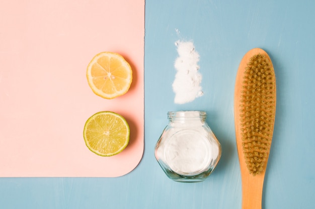 Limón, lima, refresco espolvoreado, un tarro de refresco y un cepillo de madera para limpiar sobre una superficie azul.