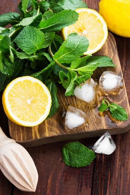 Limón, menta, hielo en una tabla de cortar de madera sobre un fondo de madera