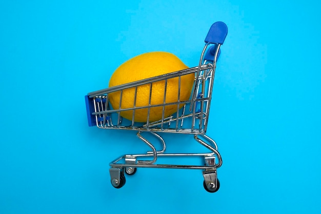 Limón en un mini carrito de supermercado sobre fondo azul Concepto de compras en línea