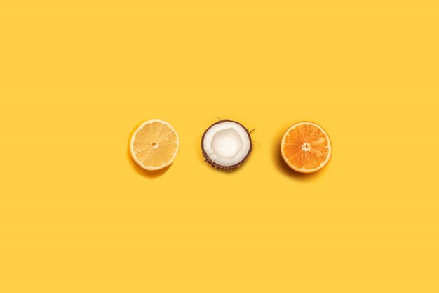 Limón, naranja y coco sobre un fondo amarillo.