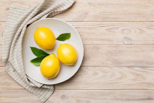 Limón recién cortado y limones enteros sobre un plato redondo sobre fondo de color Ingredientes de comida y bebida preparando una alimentación saludable tema vista superior con espacio de copia