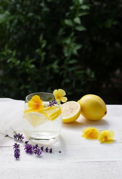 Limonada caseira em um copo na mesa de madeira branca com flores amarelas e lavanda com tecido de tule no fundo