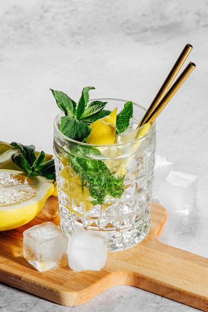 Limonada casera en elegante vaso con hielo sobre tabla de cortar de madera sobre fondo de mármol blanco