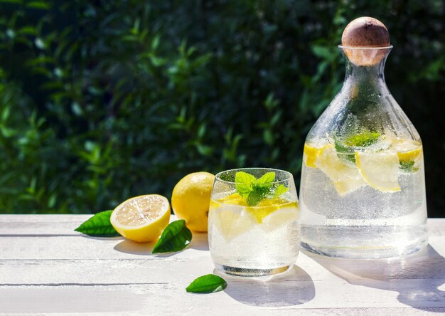 Limonada casera con menta de limón y cubitos de hielo en una jarra de vidrio sobre la mesa de madera blanca con limones