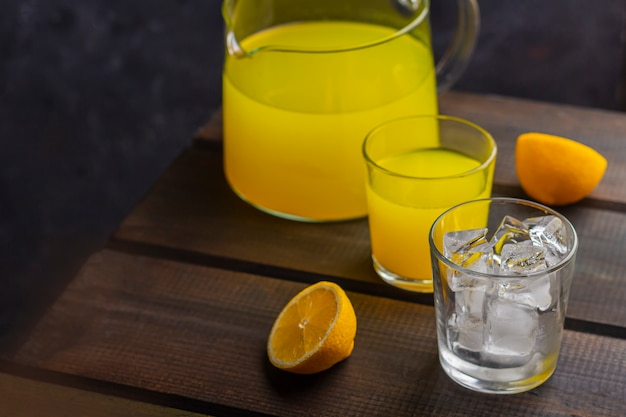 Limonada cítrica refrescante caseira no jarro e no copo e copo com cubos de gelo em um fundo de madeira. Suco de laranja fresco. O conceito de bebida orgânica e vitaminas frescas