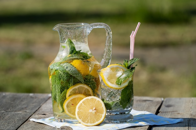 Limonada com limão, hortelã e gelo, em um jarro e uma jarra sobre a mesa de madeira velha