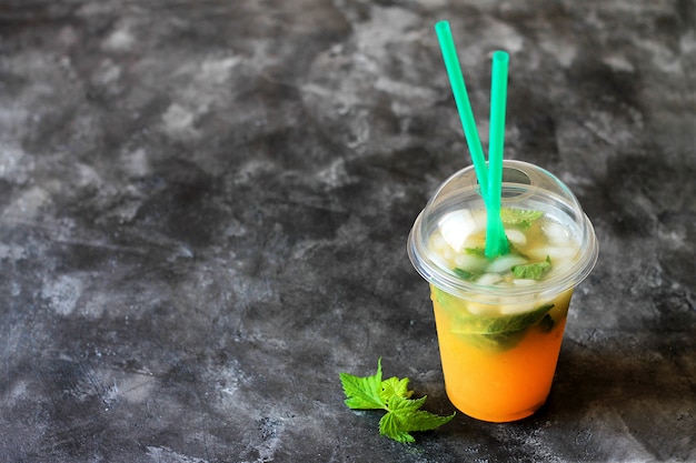 Limonada da bebida do verão com laranja e hortelã no copo plástico em um fundo escuro.