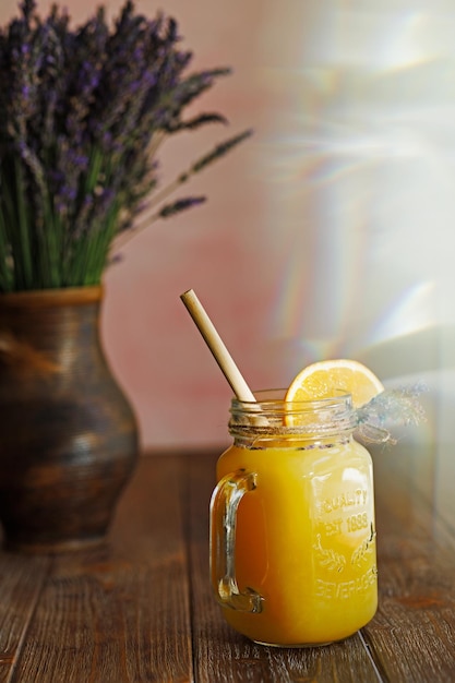 Limonada de laranja em uma caneca e um vaso com um buquê de lavanda em uma mesa de madeira