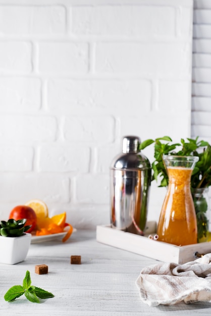 Limonada de laranja no decantador em uma bandeja de madeira e coqueteleira