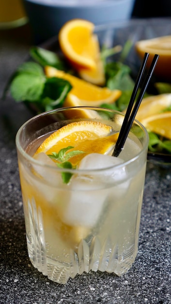 Limonada de limão com hortelã e gelo em um copo com tubos de plástico pretos sobre fundo de frutas Refrigerante bebida de verão Vertical close up