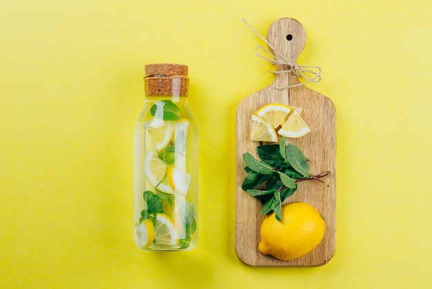 Foto limonada de limão em garrafa de vidro e ingredientes em tábuas de madeira sobre fundo amarelo