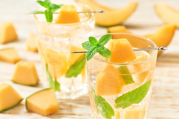 Limonada de melão com gelo e hortelã em um copo sobre uma mesa de madeira. Melão bebida em copos com fatias de melão.