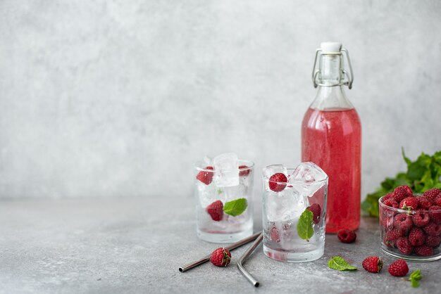 Limonada de frambuesa casera en una botella y vasos con hielo sobre una mesa blanca