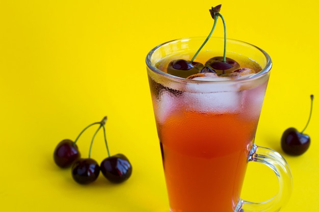 Limonada gelada com cerejas no copo no fundo amarelo. Copie o espaço.