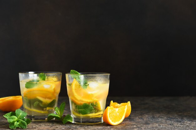 Limonada gelada com limão, laranja e hortelã em uma mesa de concreto.