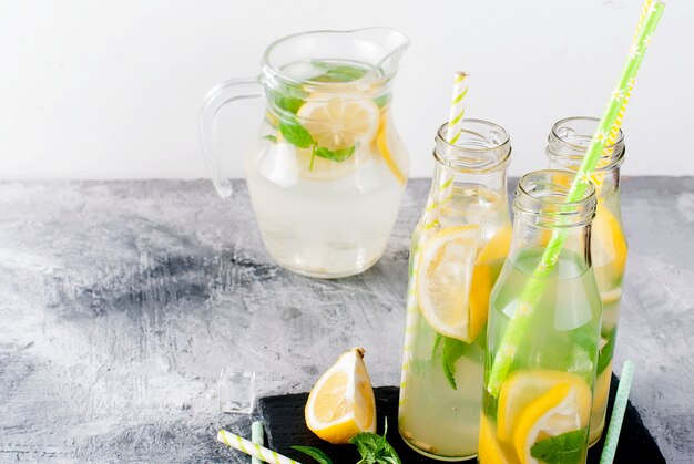 Limonada en jarra de vidrio y botellas con hielo y menta