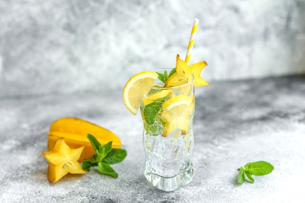 Limonada con limón, menta y cubitos de hielo en vaso sobre muro de piedra gris