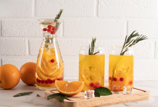 Limonada de naranja y bayas en dos vasos modernos en forma de lata y jarra sobre una mesa contra una pared de ladrillos