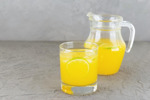 Limonada de naranja casera en un vaso y una jarra sobre un fondo gris