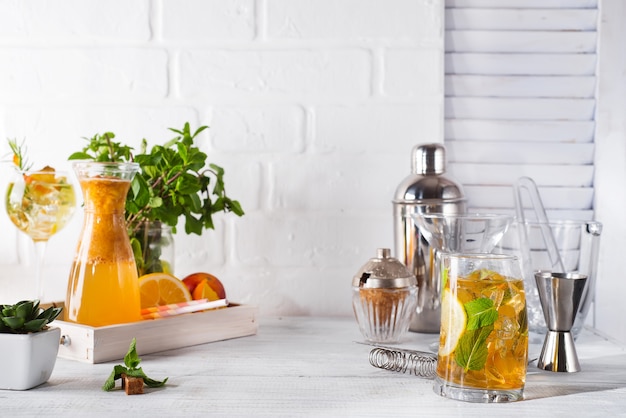 Limonada de naranja en el decantador, copa de cóctel con hielo, menta y jengibre.