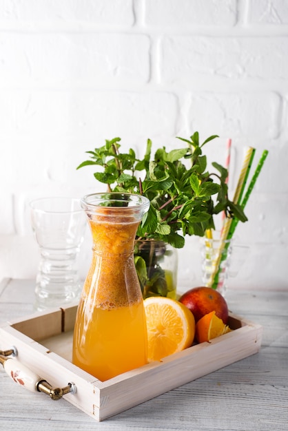 Limonada de naranja en la jarra en una bandeja de madera con pieles y menta