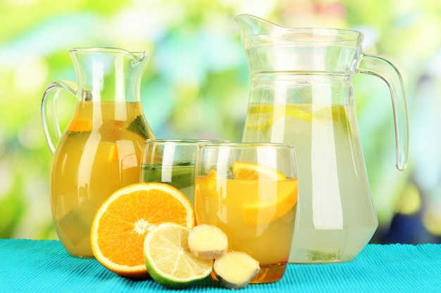 Limonada de naranja y limón en jarras y vasos sobre mesa de madera sobre fondo natural