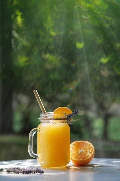 Limonada naranja en una taza sobre la mesa contra el fondo de la vegetación a la luz del sol