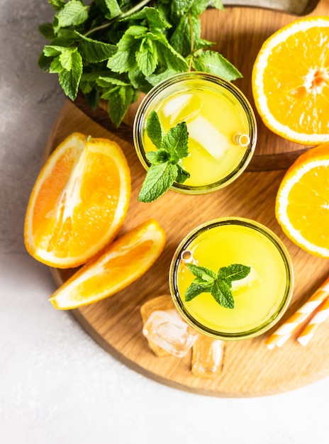 Limonada de naranja en vaso con naranja fresca y menta sobre mesa de piedra gris claro. Bebida refrescante de verano. Bar de cócteles